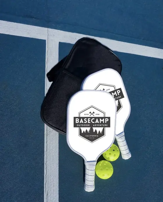 Two Basecamp branded pickleball paddles with a cover and balls on a court